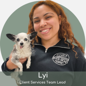 A smiling woman with curly hair in a River Road Veterinary Hospital fleece holds a small, happy dog. Text reads: “Lyi, Client Services Team Lead.”.