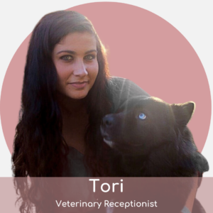 A woman with long dark hair sits beside a black dog with a blue eye, both looking toward the camera. A pink circle background and text below read: "Tori, Veterinary Receptionist.